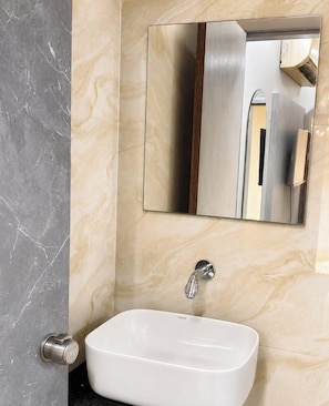 A bathroom with a white sink, a mirror, and a marble wall. - Hotel sun sai (Ahmedabad,)