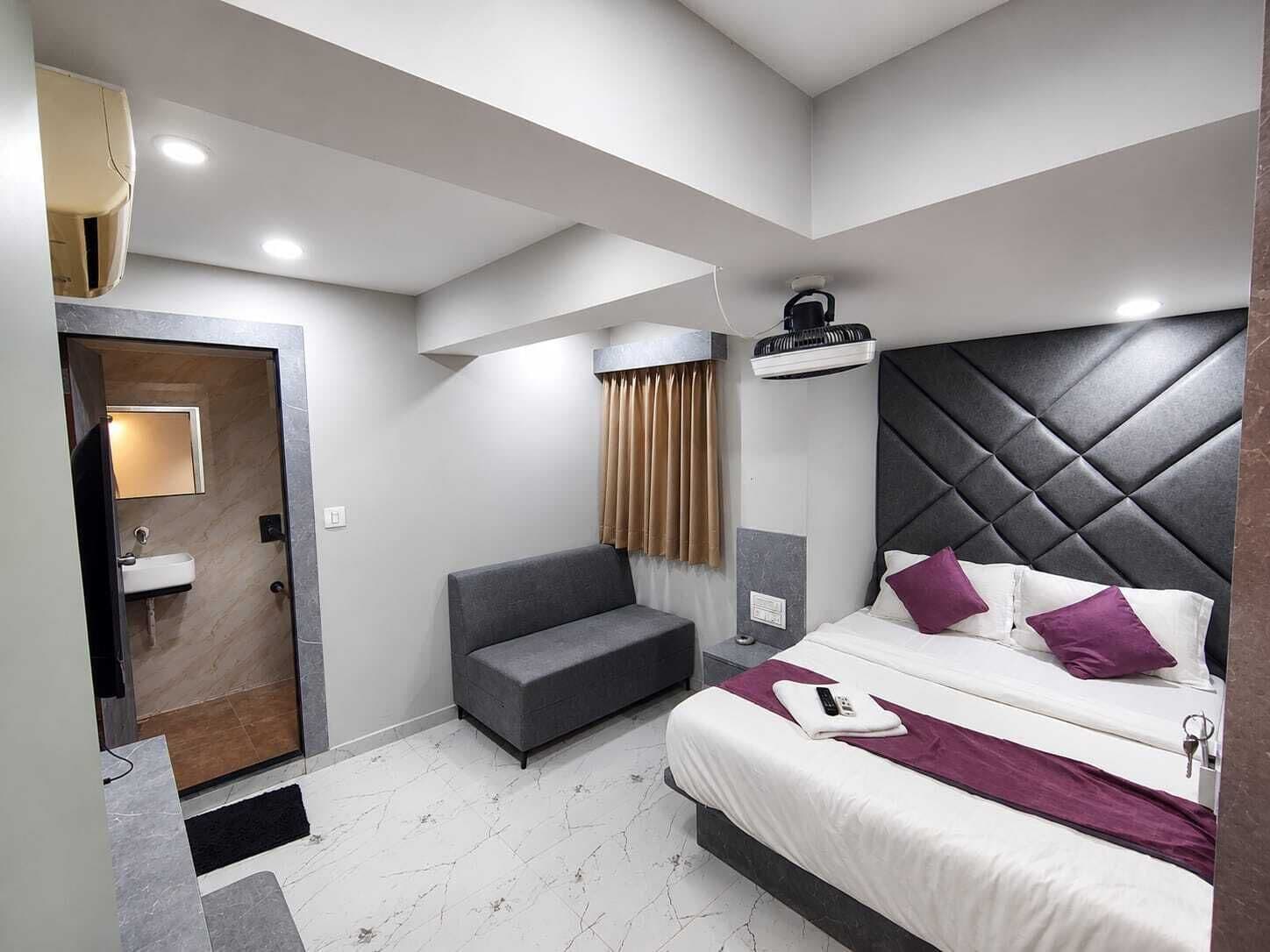 A modern hotel room with a bed, a sofa, a bathroom, and a ceiling fan.