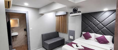 A modern hotel room with a bed, a sofa, a bathroom, and a ceiling fan.