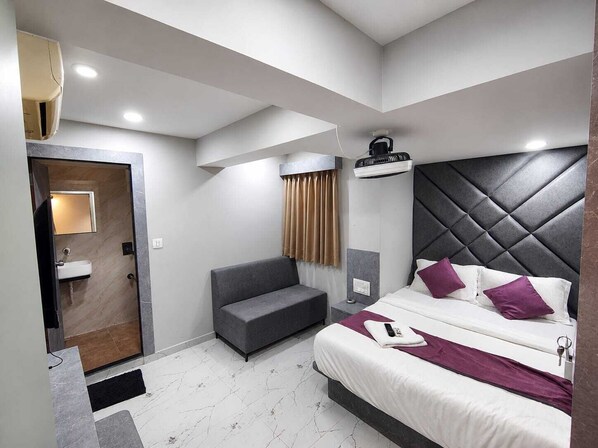 A modern hotel room with a bed, a sofa, a bathroom, and a ceiling fan. - Hotel sun sai (Ahmedabad)