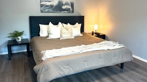 Un dormitorio con cama, mesita de noche, lámpara y un cuadro colgado en la pared.