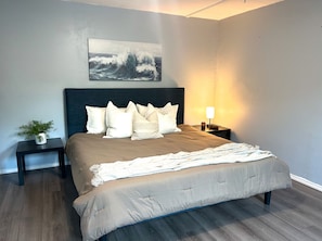 A bedroom with a bed, a bedside table, a nightstand, a lamp, and a wall-mounted painting. - Cozy Multi-Bedroom Getaway Near Kern River, CA (Bodfish)