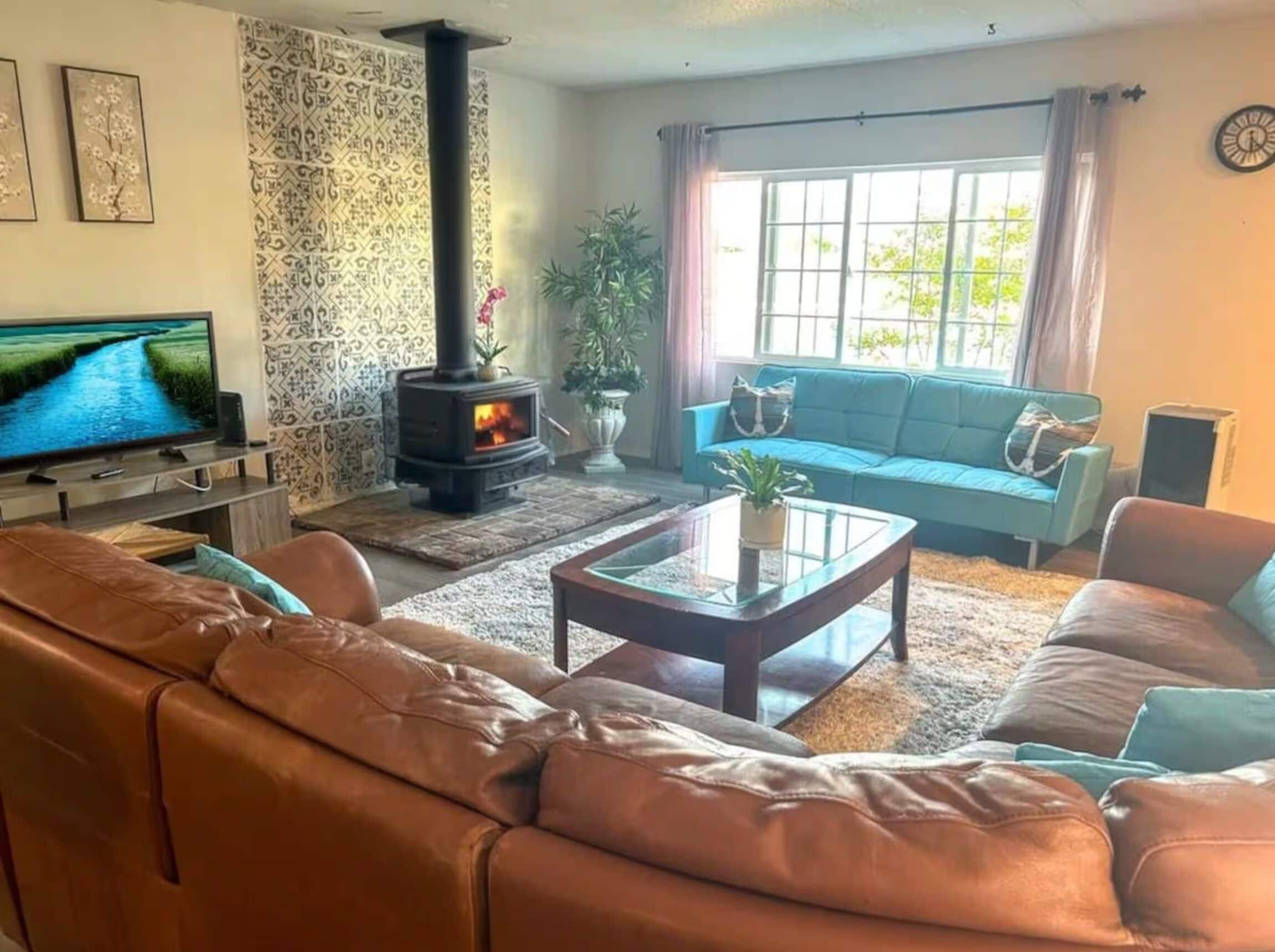 Ein Wohnzimmer mit Sofa, Couchtisch, Fernseher, Kamin und einem Fenster mit Vorhängen.