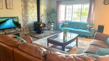 Ein Wohnzimmer mit Sofa, Couchtisch, Fernseher, Kamin und einem Fenster mit Vorhängen.