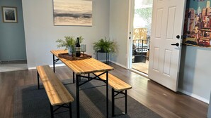 Un comedor con una mesa de madera y bancos, un cuadro en la pared y una puerta que da al exterior.