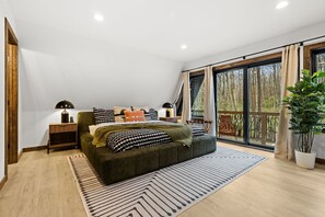 Ein Schlafzimmer mit einem Bett, Nachttischen, einem Fenster mit Vorhängen und Blick auf Bäume.