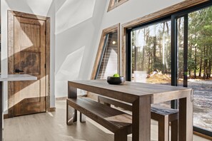Ein modernes Interieur mit einem Holztisch und einer Bank, einem großen Fenster mit Blick auf Bäume und einer Tür mit Holzrahmen.