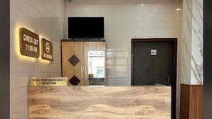 Bancada de recepção com superfície semelhante a mármore, tapete vermelho e placa indicando o horário de check-out.