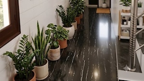 Um corredor com plantas em vasos, piso de mármore e escada com corrimão de metal.