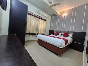 Una habitación de hotel con cama, televisión de pantalla plana, aire acondicionado y ventilador de techo.