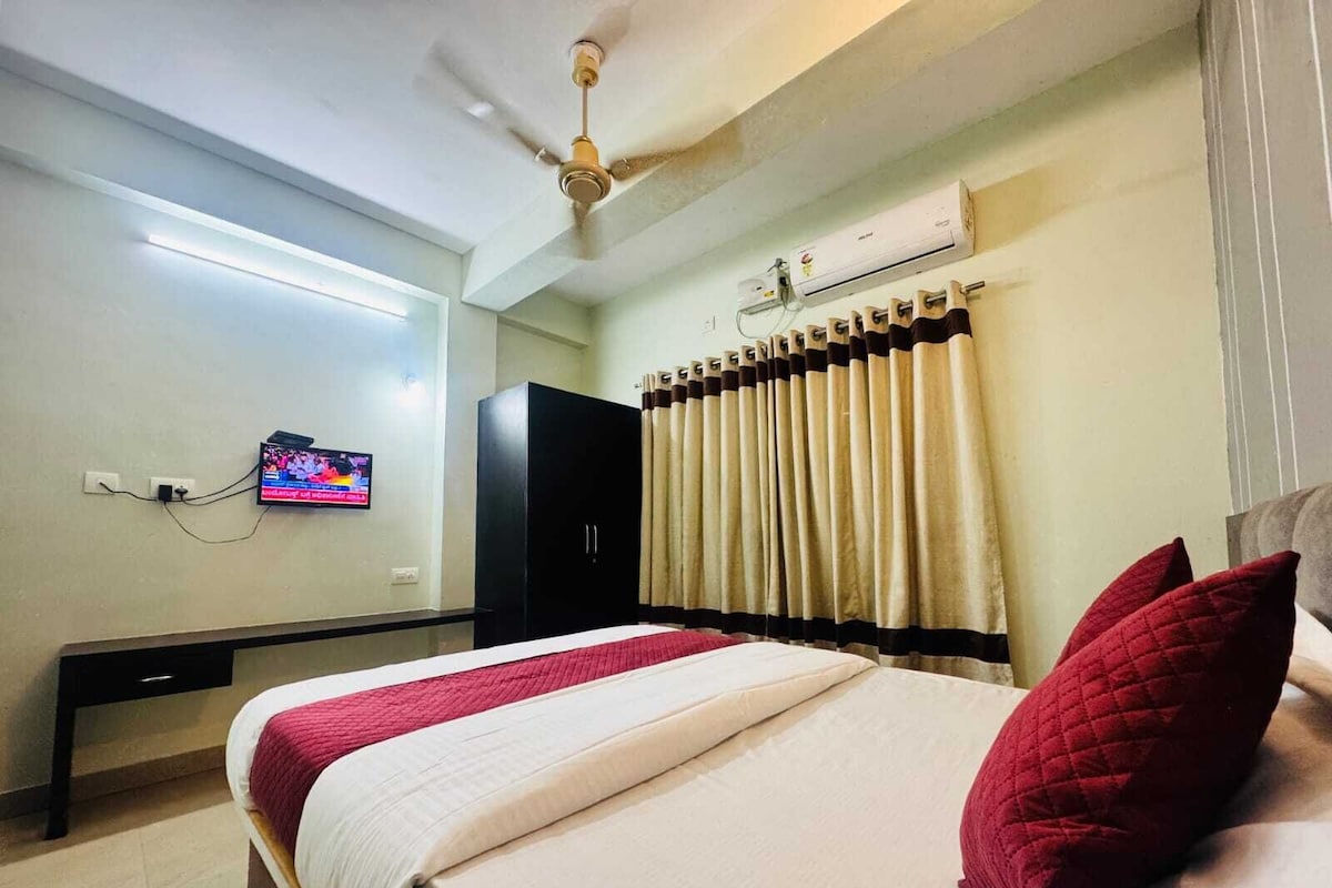 Habitación de hotel con cama, televisor montado en la pared, ventilador de techo y aire acondicionado.
