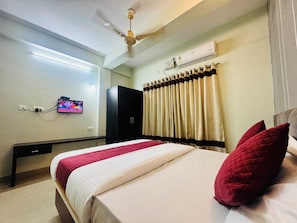 Habitación de hotel con cama, televisor montado en la pared, ventilador de techo y aire acondicionado.