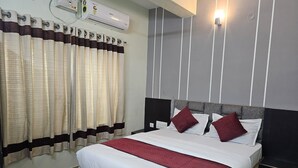 A hotel room with a bed, curtains, an air conditioning unit, and a wall-mounted light fixture. - Sri Chaitanya Residency  (Mysore)