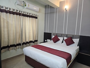 Habitación de hotel con cama, cortinas, equipo de aire acondicionado y lámpara de pared.