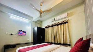 A hotel room with a bed, a TV mounted on the wall, a ceiling fan, and an air conditioning unit. - Sri Chaitanya Residency  (Mysore)