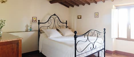 A bedroom with a bed, a nightstand, a vase with flowers, and a window.