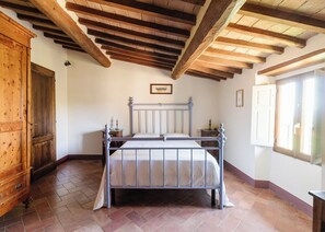 Een slaapkamer met een houten plafond, een bed met metalen frame, een houten garderobe en een raam.
