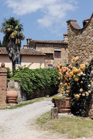 A rustic stone building with a tiled roof, a palm tree, and a garden with yellow and white flowers. - Casa Sornano, an apartment with a view of Chianti (Toscana)