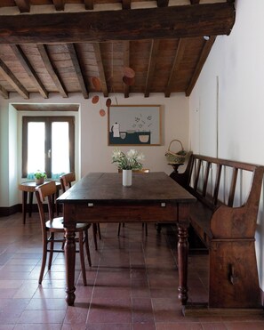 A dining area with a wooden table, chairs, a bench, and a painting on the wall. - Casa Sornano, an apartment with a view of Chianti (Toscana)