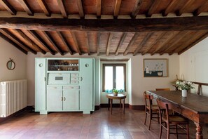 Een landelijke keuken met een houten plafond, een lichtblauwe kast, een eettafel met stoelen en een raam met gordijnen.