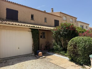 A residential building with a tiled roof, a garage door, and a small garden area with gravel and plants. - La Marianne with Sea View, Private Terrace, Air Conditioning (Fleury)