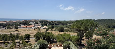 Un patio amueblado al aire libre, rodeado de vegetación y con vistas a un pueblo costero.