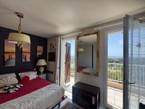 Une chambre à coucher avec un lit, une commode, un miroir et un balcon offrant une vue.
