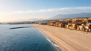 Un paisaje costero con playa, edificios y montañas al fondo.