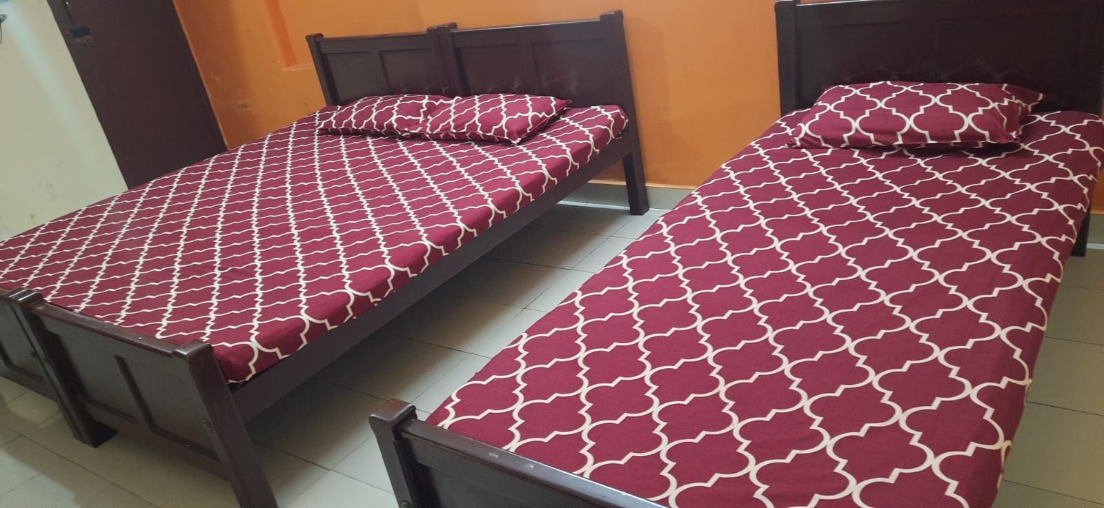 Dos camas individuales con cabeceras y pies de cama a juego, piso de baldosas y una pared lisa.