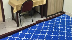 A room with a desk, chair, television, wardrobe, and a patterned carpet.