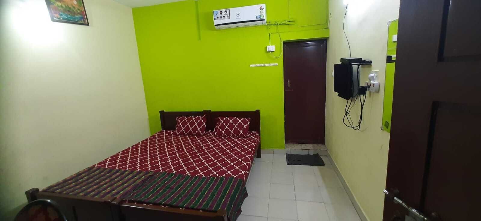 A bedroom with a bed, a wall-mounted air conditioner, a television, and a door.