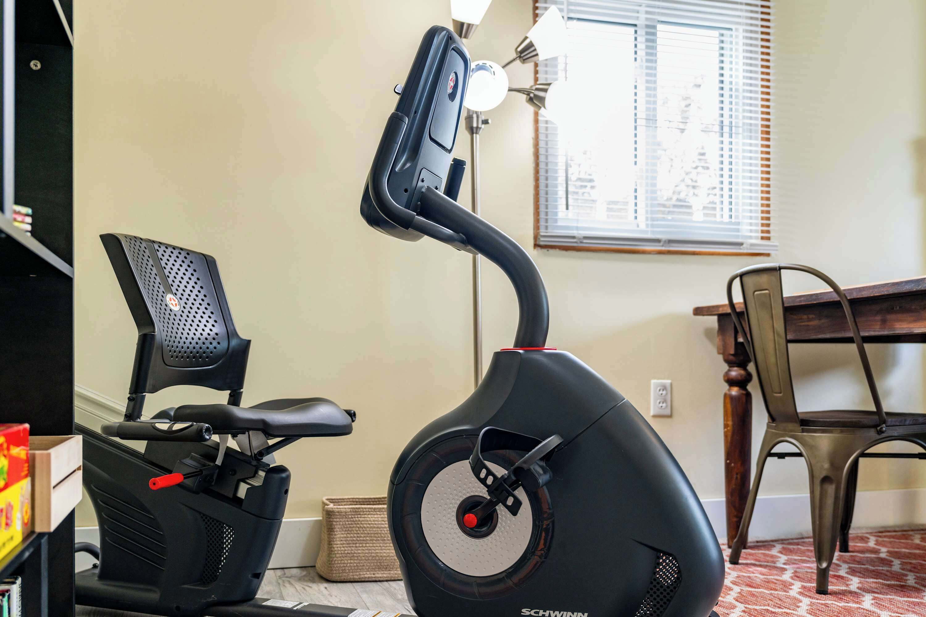 Un vélo d’appartement, une console de commande, un fauteuil de bureau noir, une table à manger et une fenêtre avec des stores.