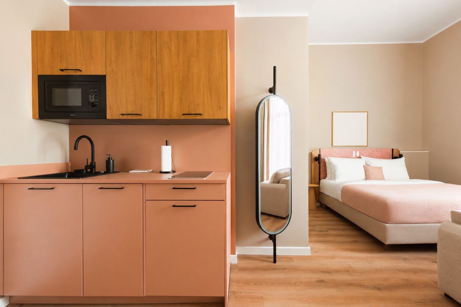 Ein modernes Hotelzimmer mit einer Küchenzeile, einem Bett, einem Nachttisch und einem Spiegel.