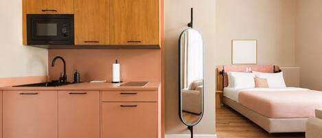 A modern hotel room with a kitchenette, a bed, a bedside table, and a mirror.