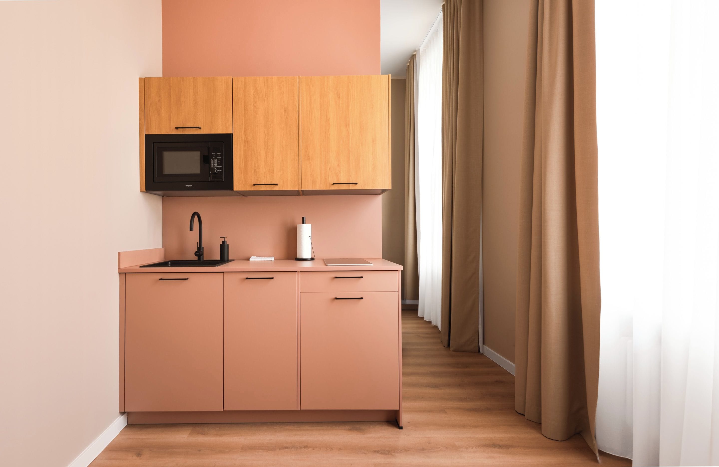 Een kleine keuken met een magnetron, spoelbak en opbergkasten.