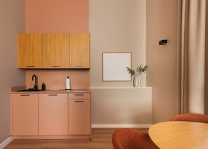 A modern kitchen with wooden cabinets, a black faucet, and a white vase with greenery on the wall. - Limehome Bremen Balgequartier (Bremen)