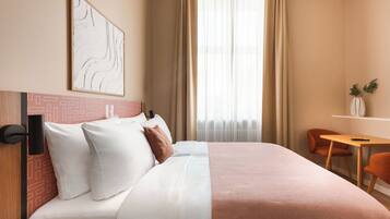 Een hotelkamer met een bed, een bureau, een stoel, een raam met gordijnen en een kunstwerk aan de muur.