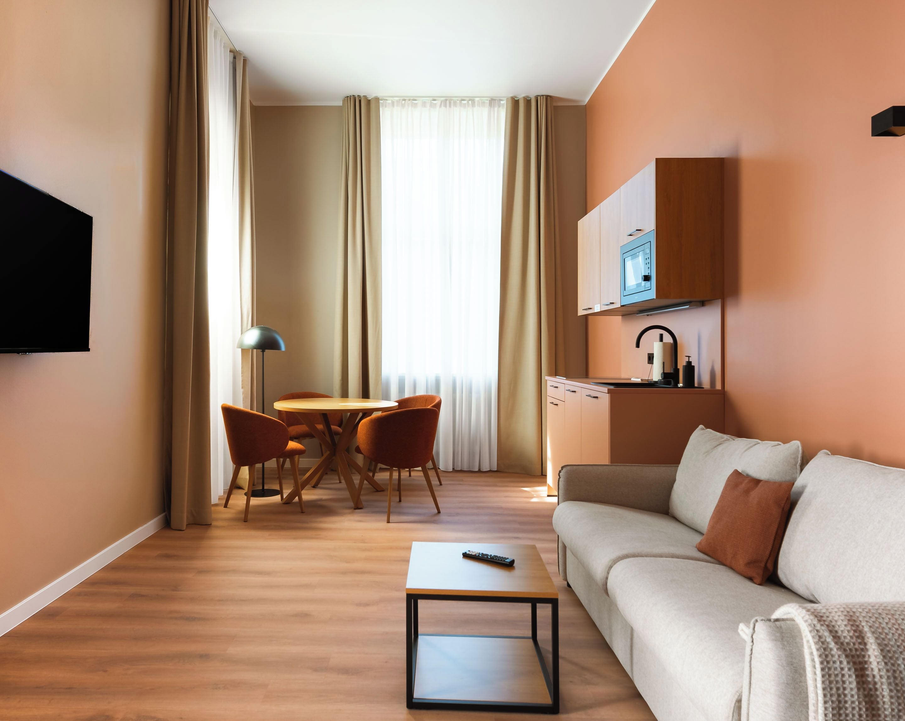 Quarto de hotel com sofá, mesa de centro, televisão, área de refeições com cadeiras e cozinha equipada com micro-ondas.
