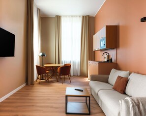 Hotellihuoneessa on sohva, sohvapöytä, televisio, ruokailualue tuoleineen sekä keittiö, jossa on mikroaaltouuni.