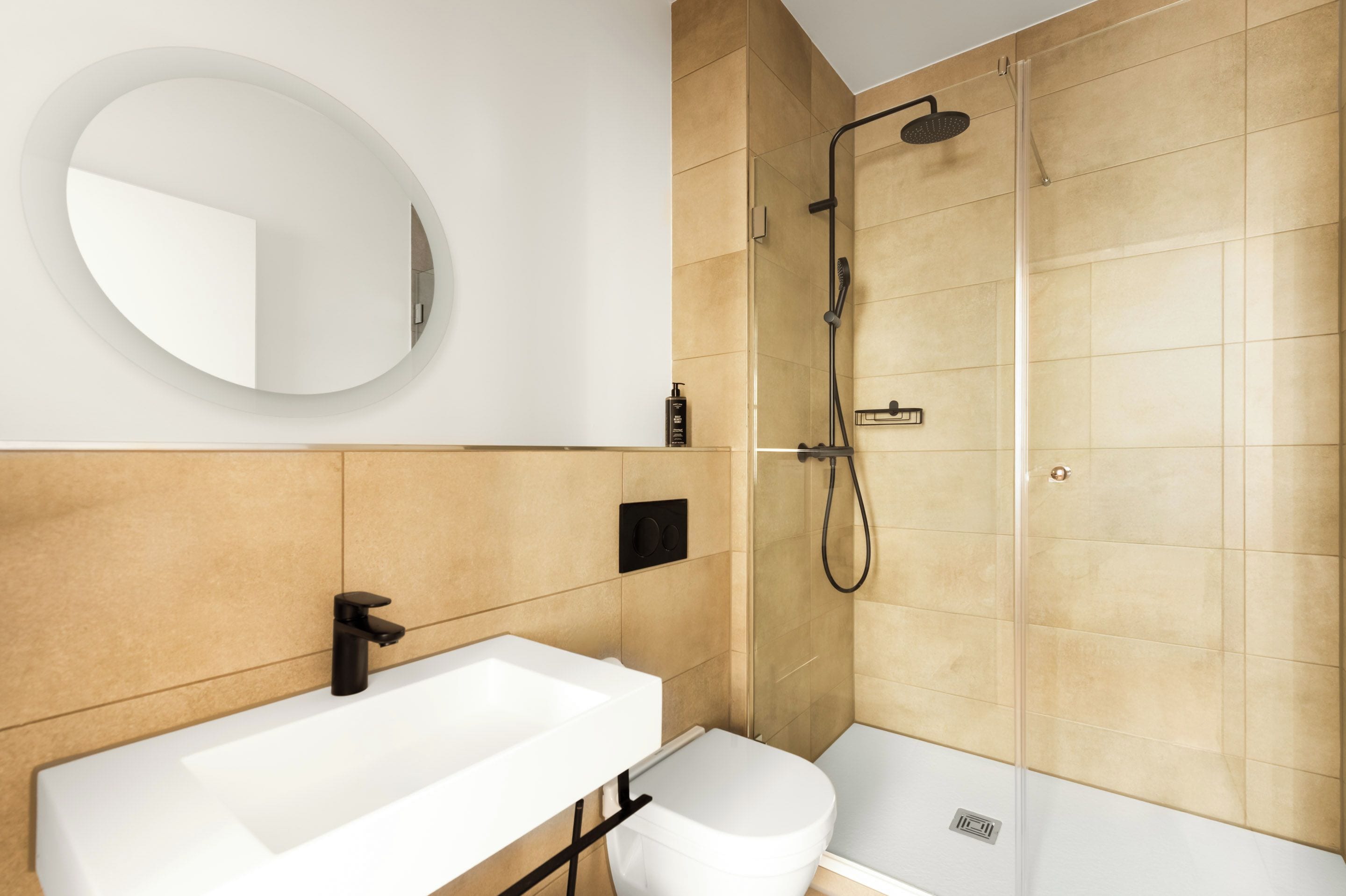 Ein modernes Badezimmer mit einem weißen Waschbecken, einem runden Spiegel und einer begehbaren Dusche.
