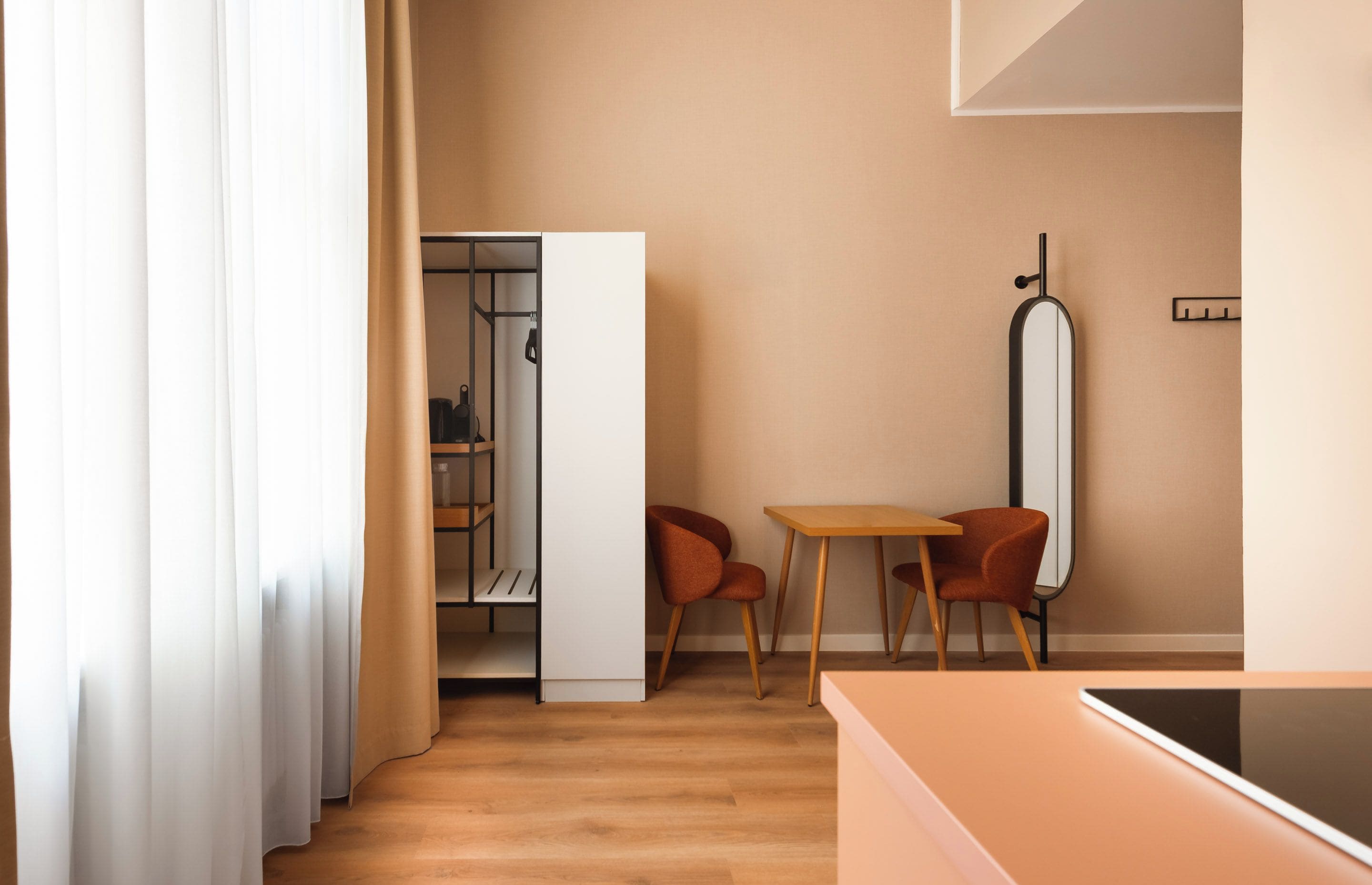 Quarto moderno com piso de madeira, uma cama, uma mesa com duas cadeiras e um guarda-roupa com espelho.