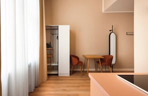 Una habitación moderna con piso de madera, una cama, una mesa con dos sillas y un armario con espejo.