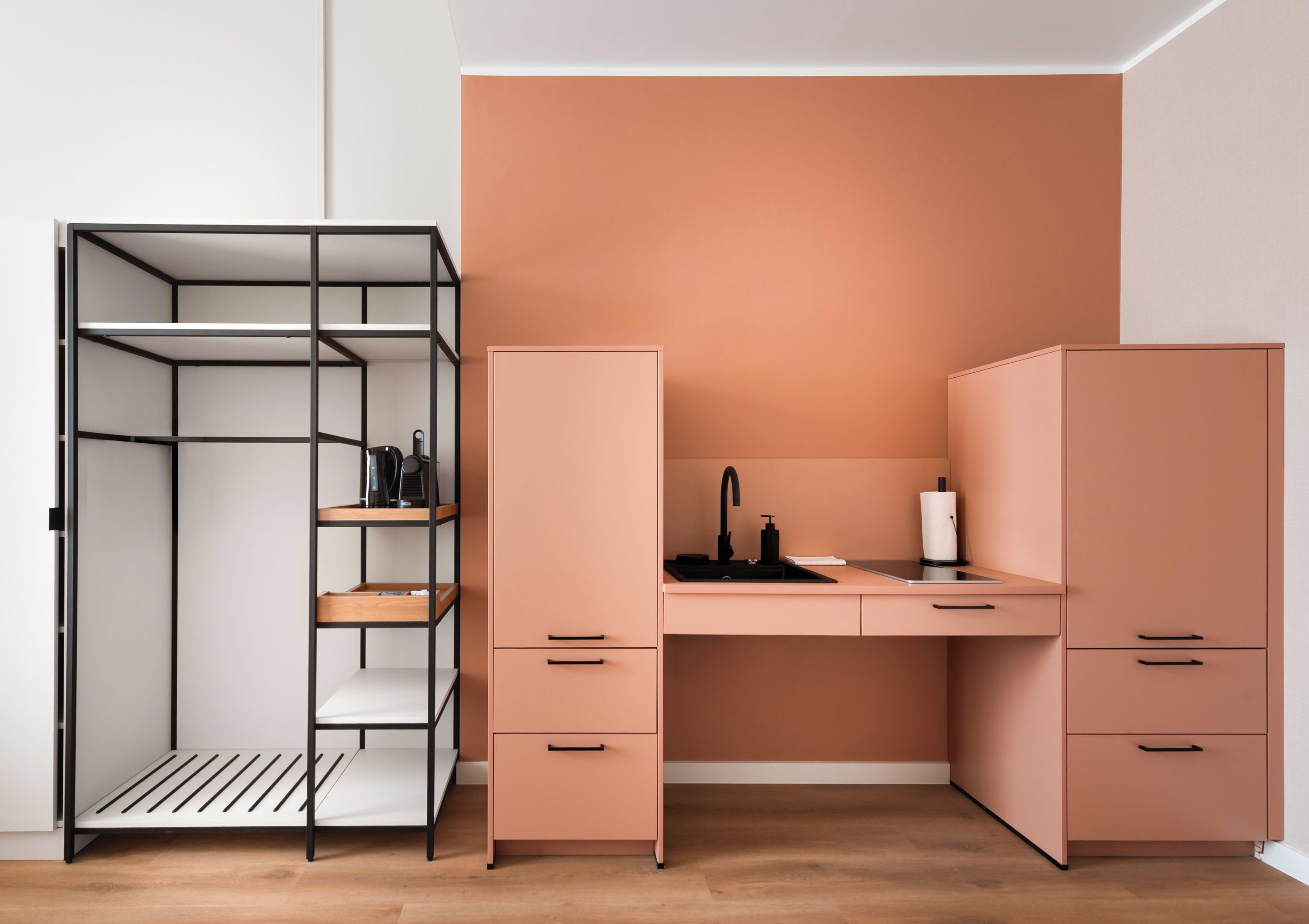 A compact bedroom with a built-in wardrobe, a desk with a sink, and a shelving unit.