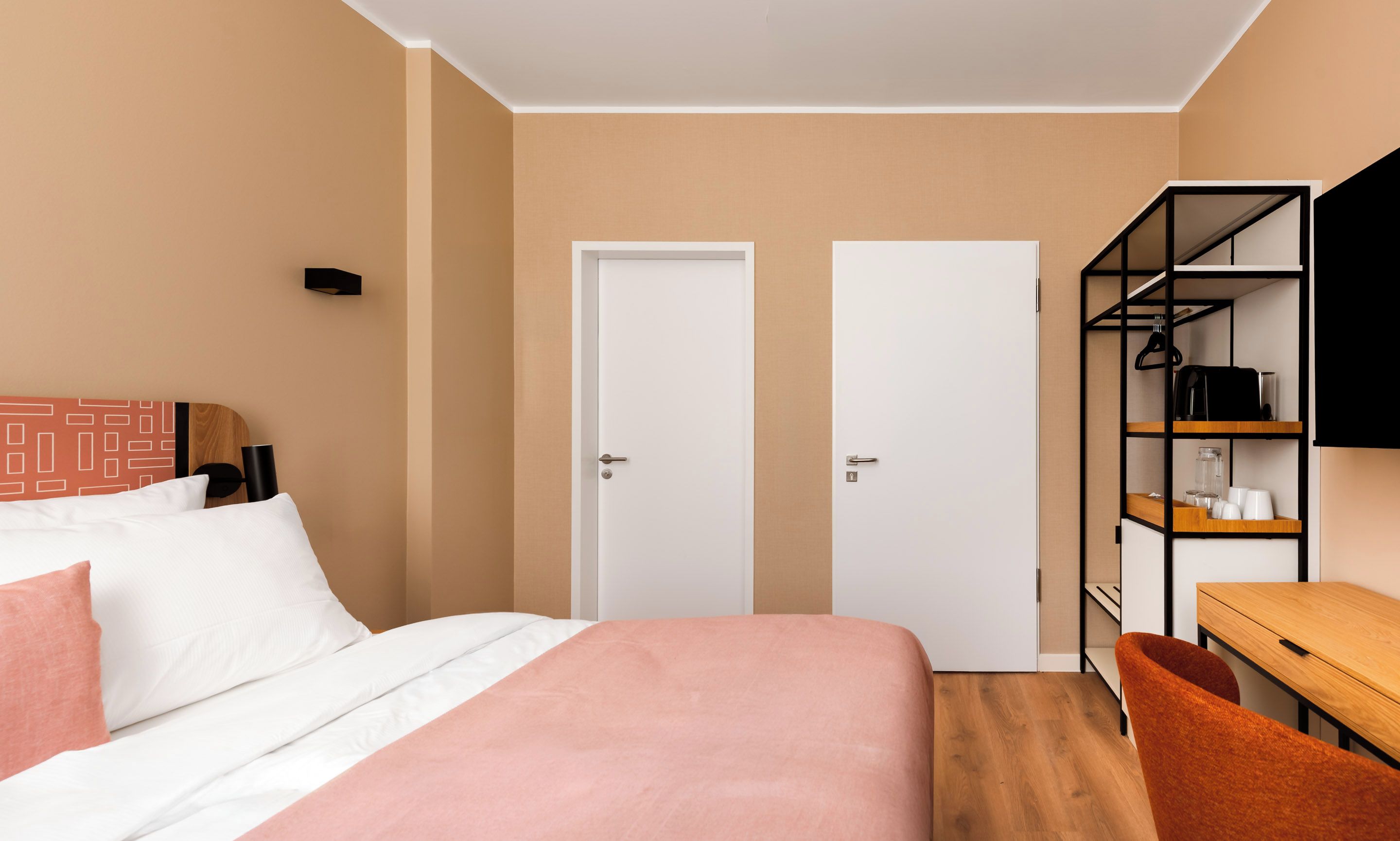 Una habitación de hotel con una cama, un escritorio, una silla y un televisor montado en la pared.