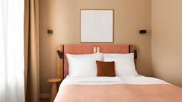 A hotel room with a bed, a headboard with a geometric pattern, a framed artwork on the wall, and a nightstand with a lamp.