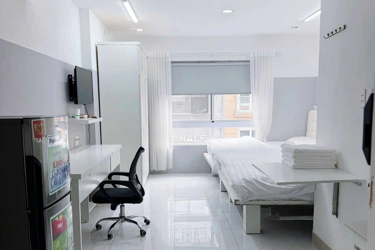 Ein Hotelzimmer mit Bett, Schreibtisch, Stuhl, Kühlschrank und einem fenster mit Vorhängen.