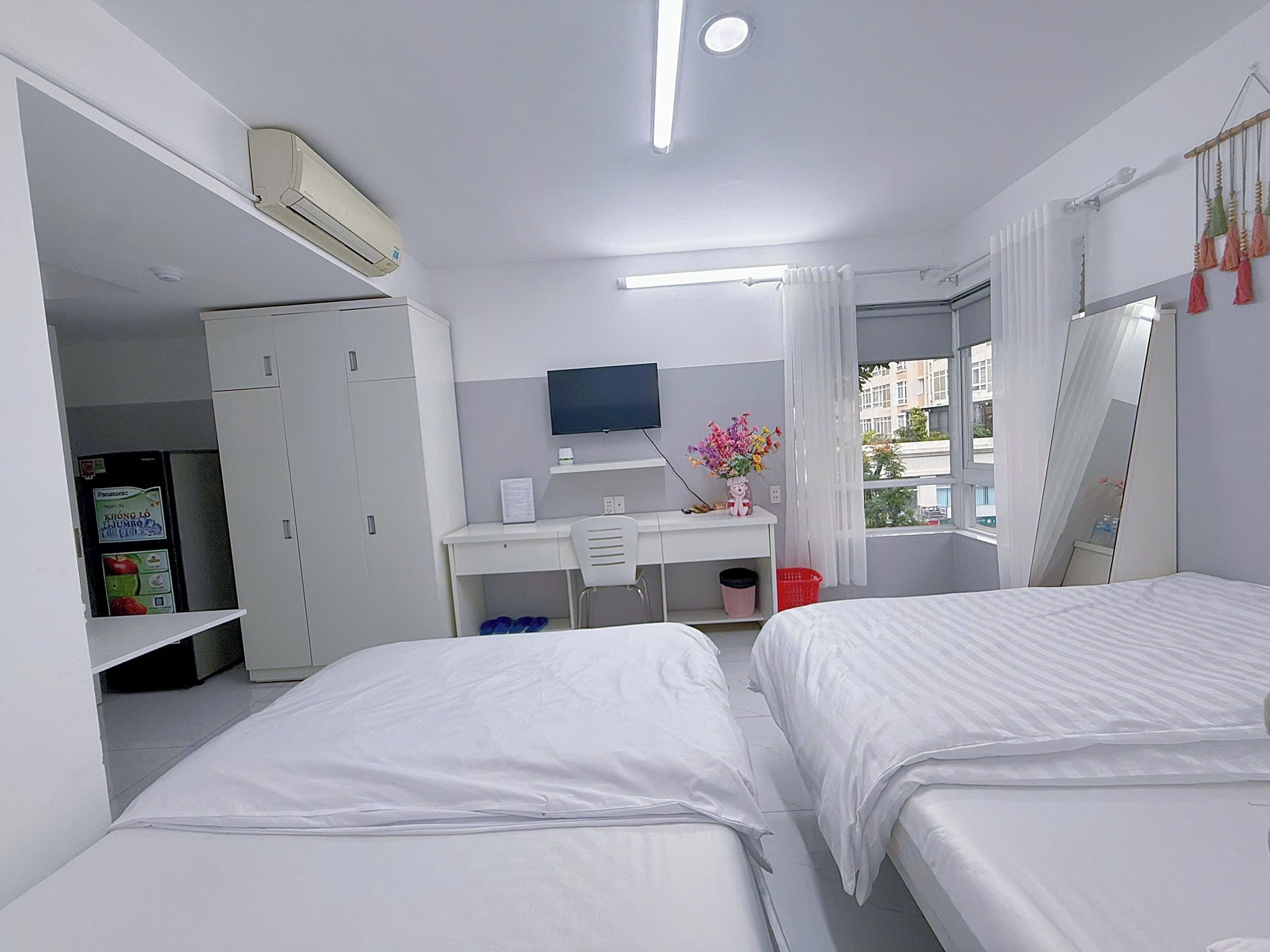 Habitación de hotel con dos camas, un escritorio, un televisor y un ventanal con cortinas.
