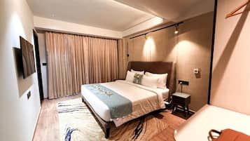 A hotel room with a large bed, a bedside table, a TV mounted on the wall, and a window with curtains.
