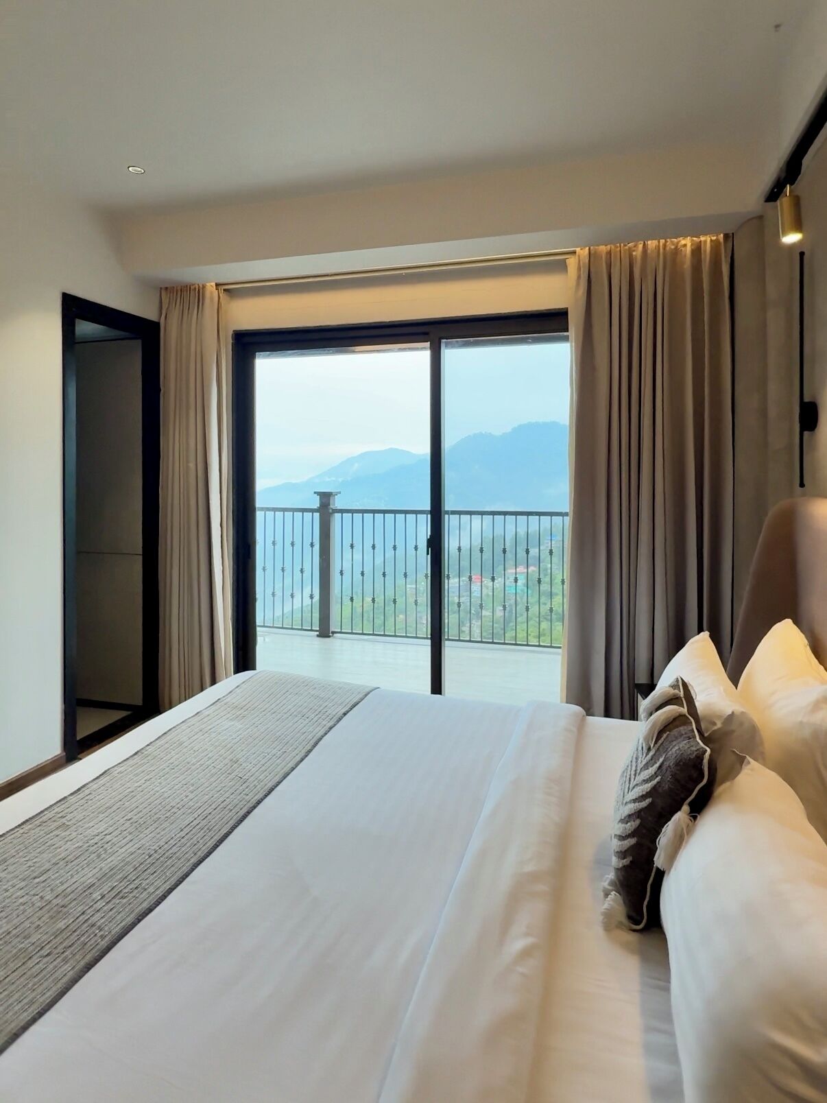 Una habitación de hotel con una cama grande, vistas a las montañas desde un balcón y una puerta corrediza.