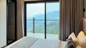 Una habitación de hotel con una cama grande, vistas a las montañas desde un balcón y una puerta corrediza.